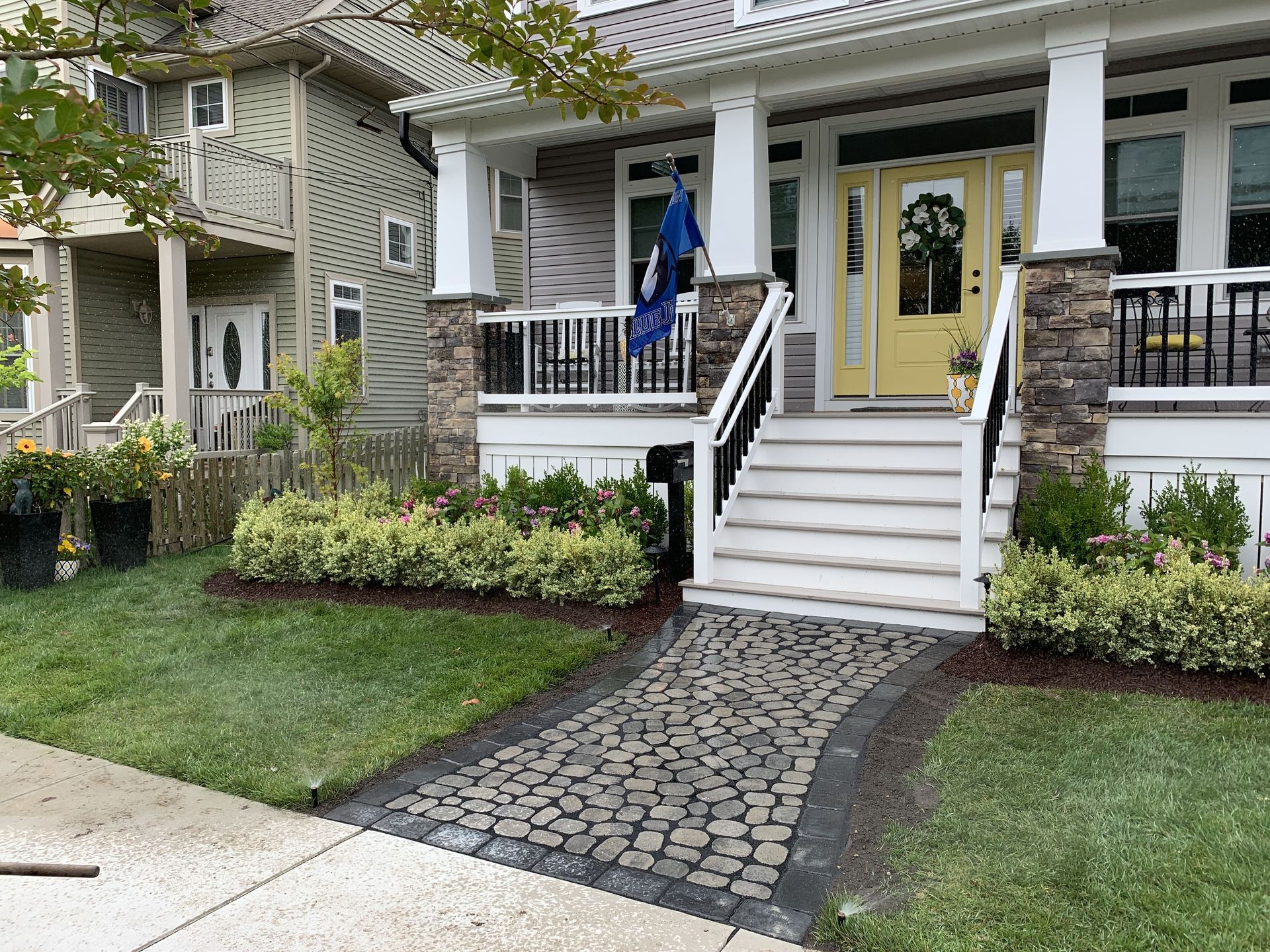 Front porch of a house with white stairs, yellow door, and a cobblestone walkway through a green lawn