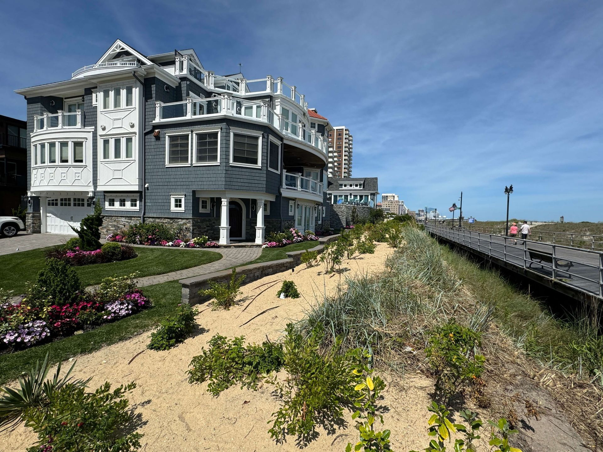 Coastal inn beside a sandy dune and boardwalk under a blue sky, with flowers along the path.