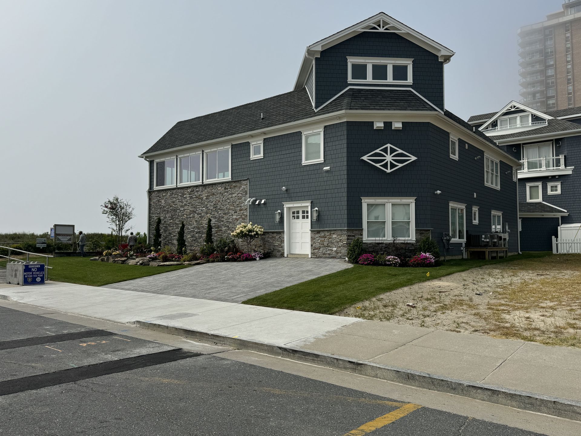 Dark blue coastal house with white trim, sloped driveway, and landscaped yard by the street