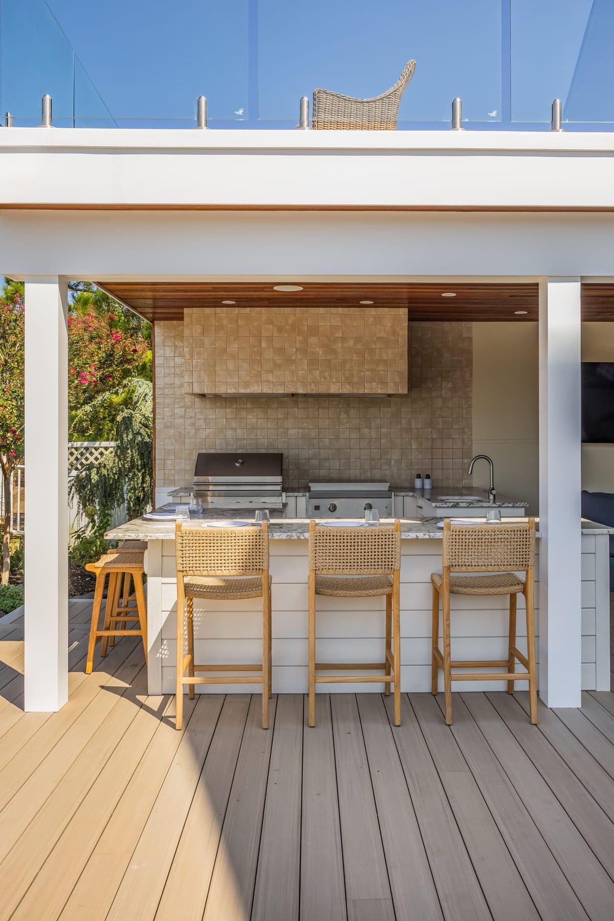 Open-air outdoor kitchen with bar stools and woven counter seats under a covered patio