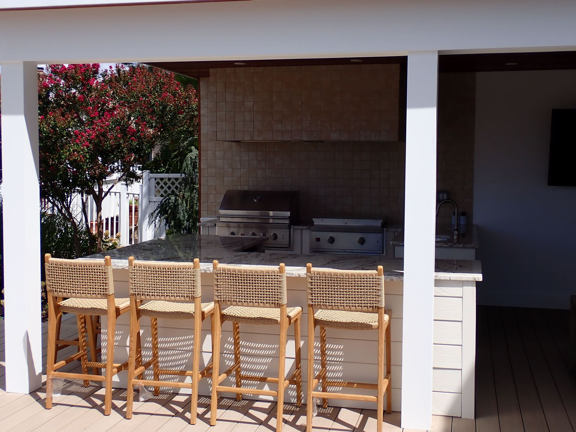 Outdoor patio with wooden barstools facing a built-in grill under a covered terrace