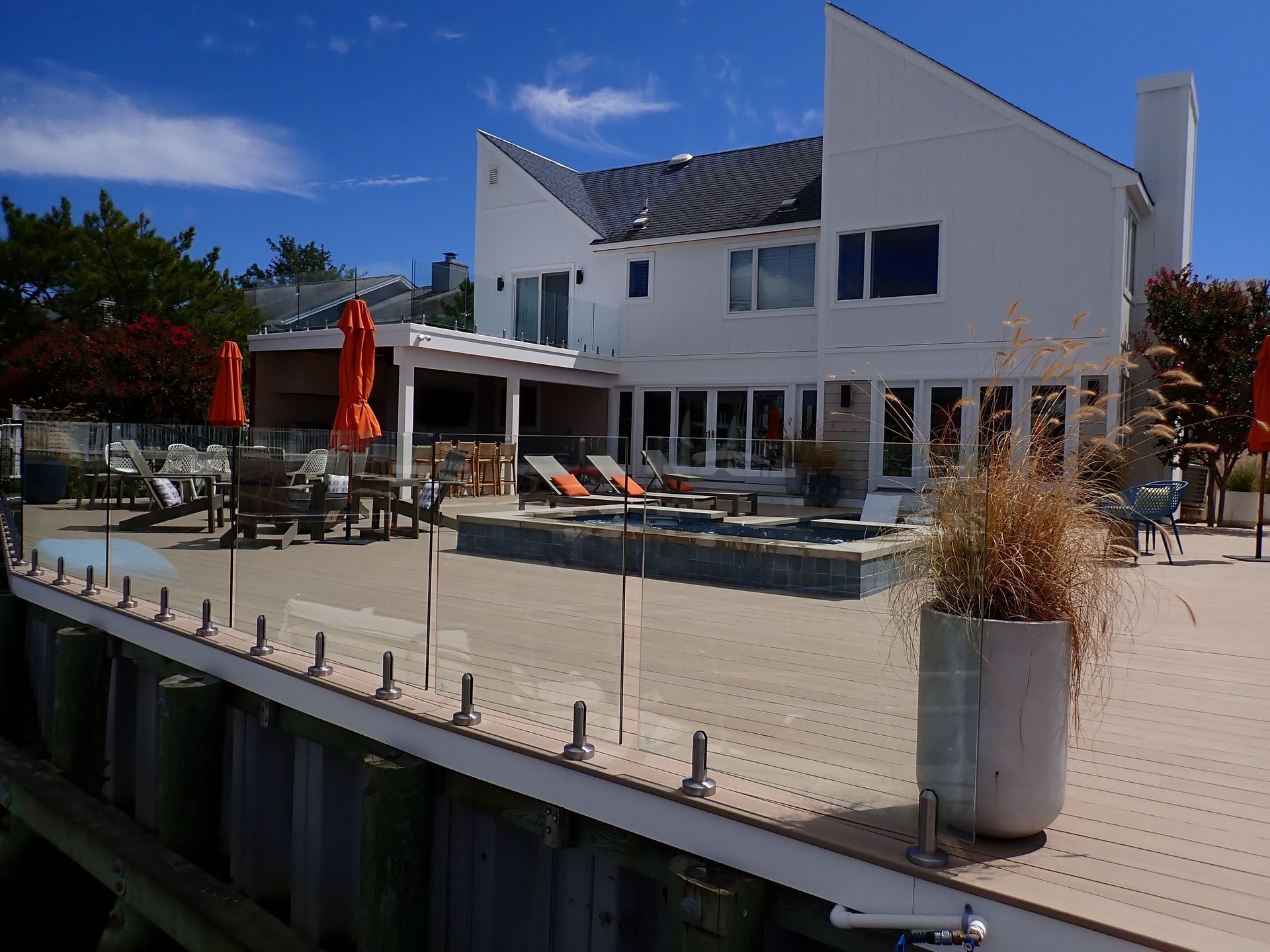 Modern white house with a patio, pool, red umbrellas, and lounge chairs under a blue sky
