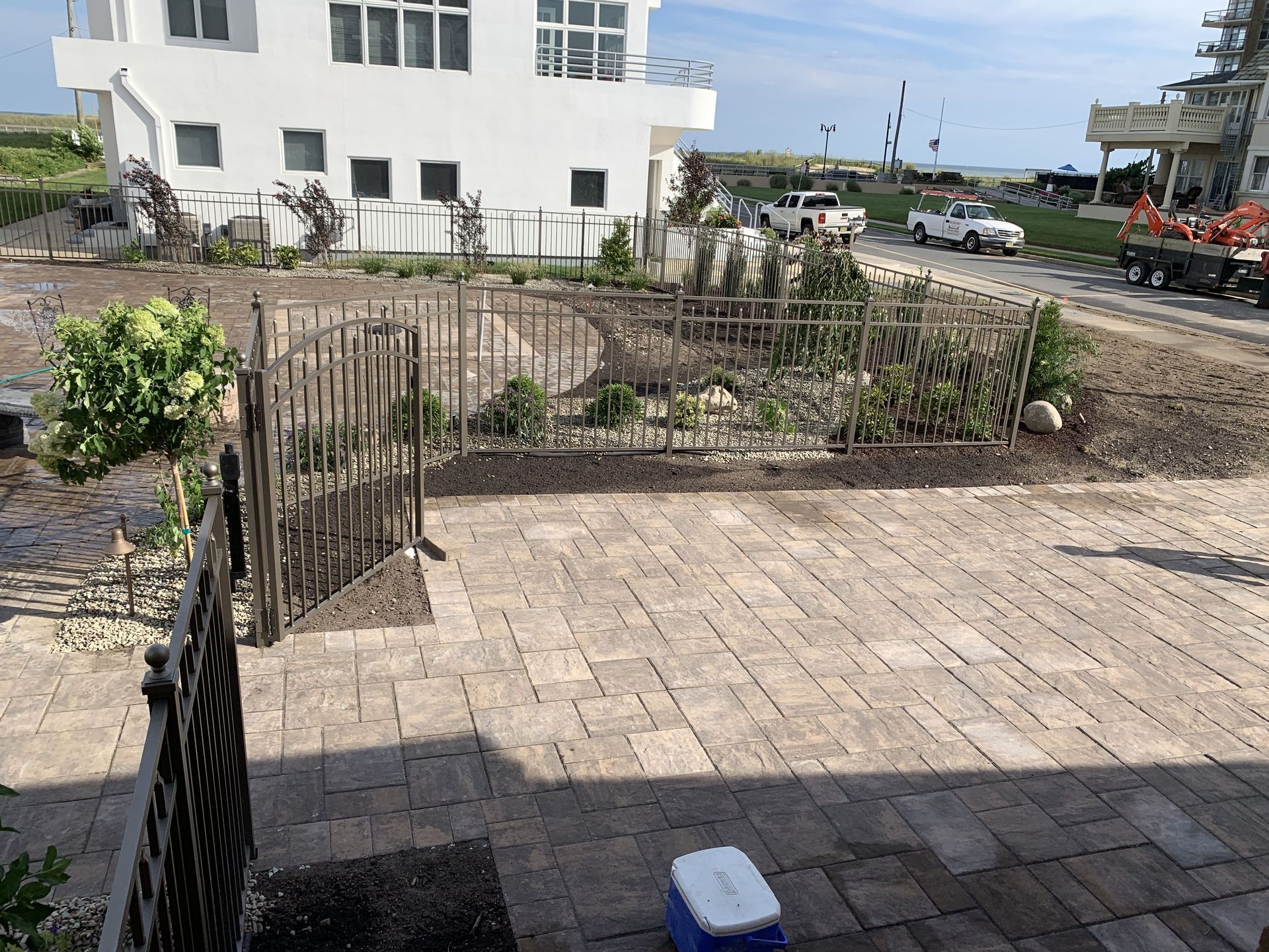 Paved courtyard beside a white building, with small fenced garden beds and a street in the background.