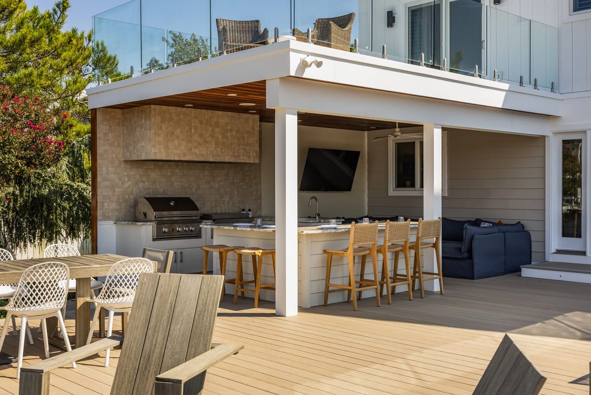 Outdoor patio with a white pergola, bar seating, lounge chairs, and a grill beside a modern house