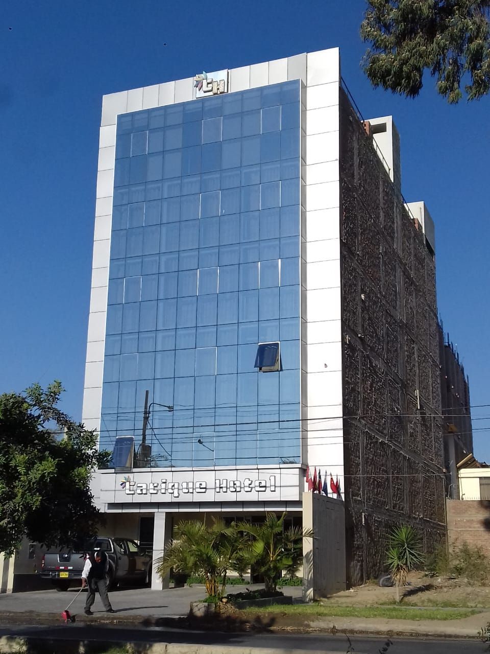 Edificio de oficinas de cristal azul con fachada blanca, letreros en árabe y árboles al frente bajo un cielo despejado.