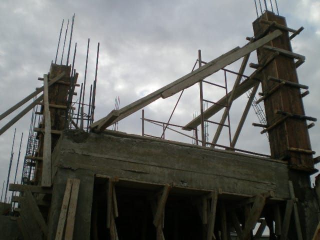 Estructura de hormigón parcialmente construida con andamios y barras de refuerzo expuestas bajo un cielo nublado.