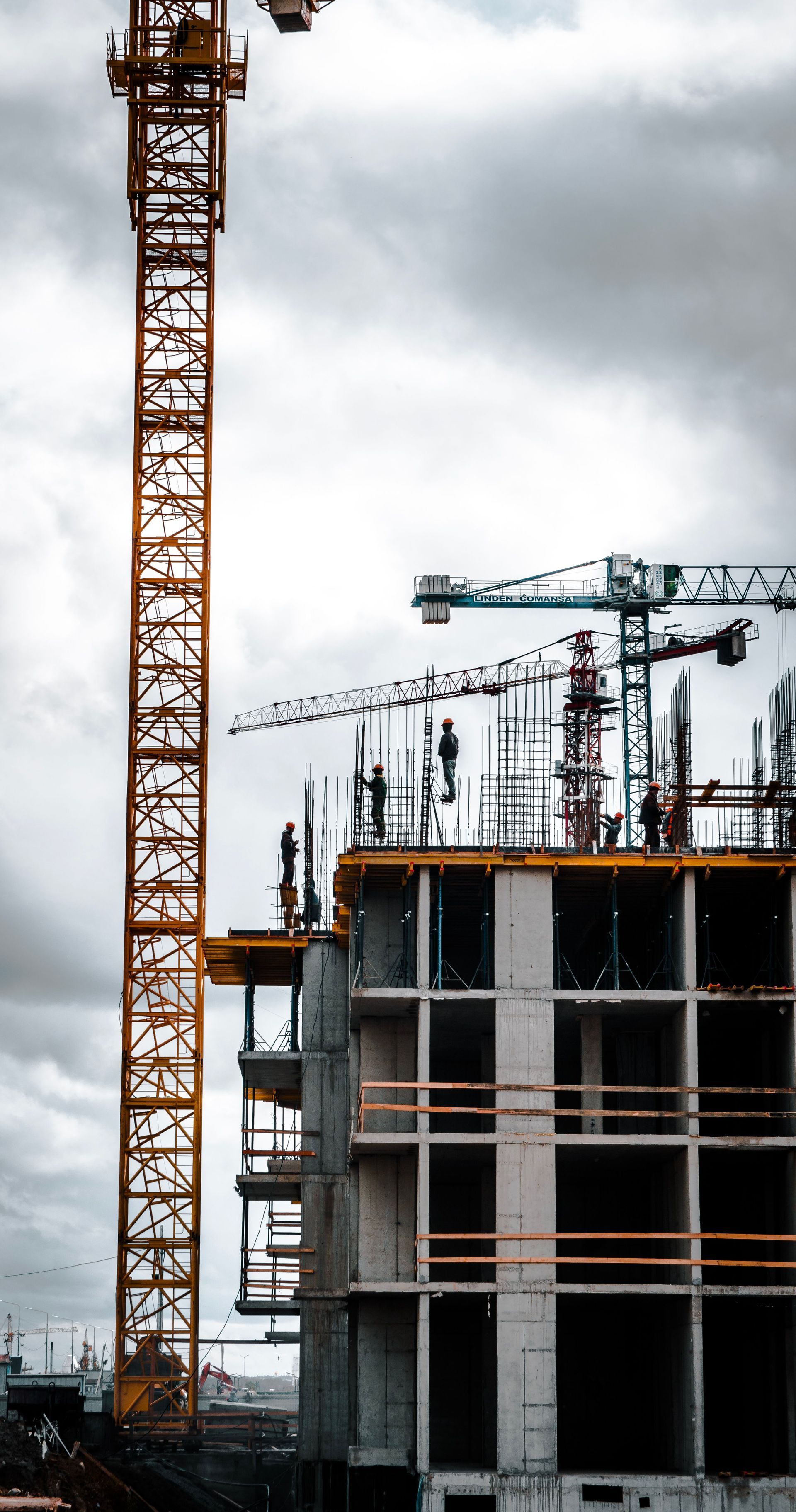 Obra en construcción con un rascacielos en construcción, grúas y un cielo nublado.
