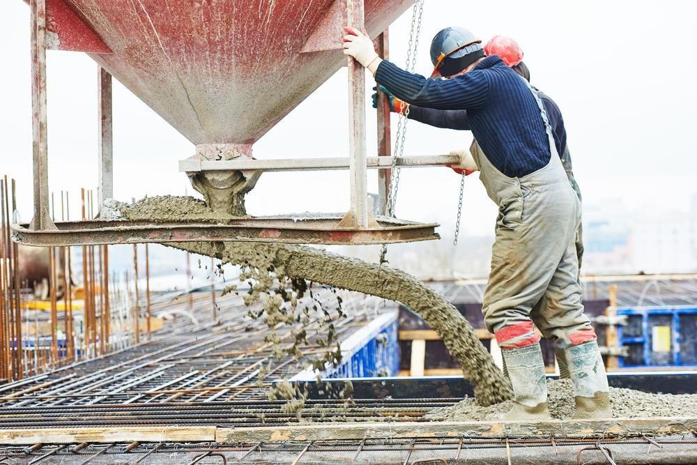 A Man Is Pouring Concrete Into a Concrete Mixer at A Construction Site — Next Level Construction Contractors in Batlow, NSW