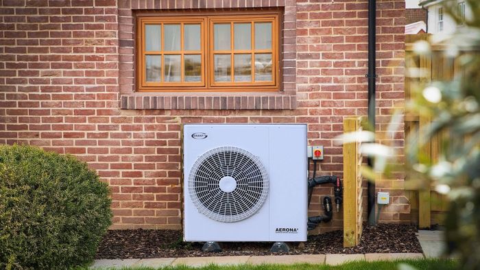Aerona heat pump outside a kitchen window between a bush and a tree