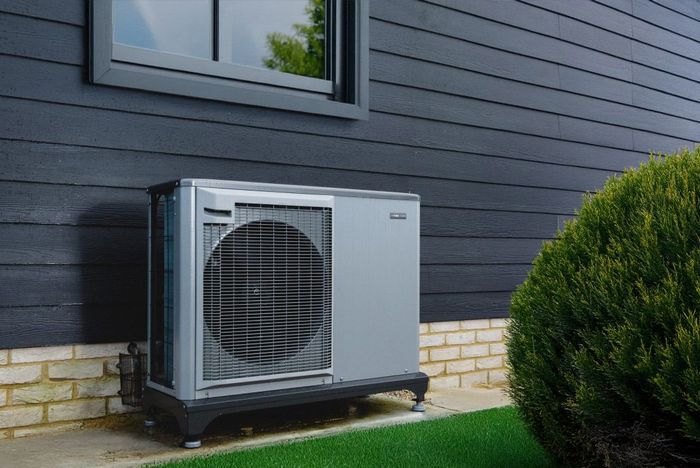 Heat pump on a grass path next to a bush