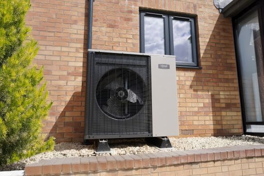 Heat pump outside the back door of a brick house, next to a bush