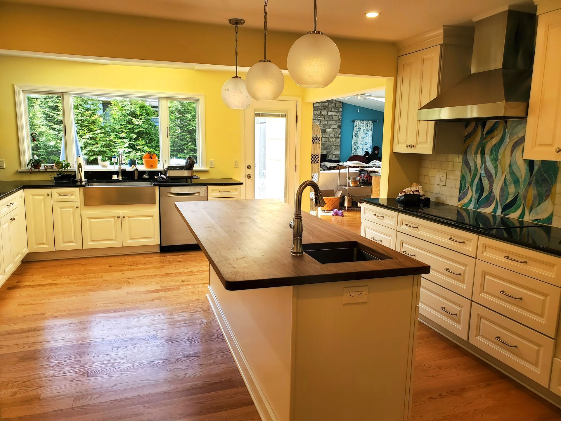 Bright modern kitchen with white cabinets, island, wood floors, and large windows overlooking greenery
