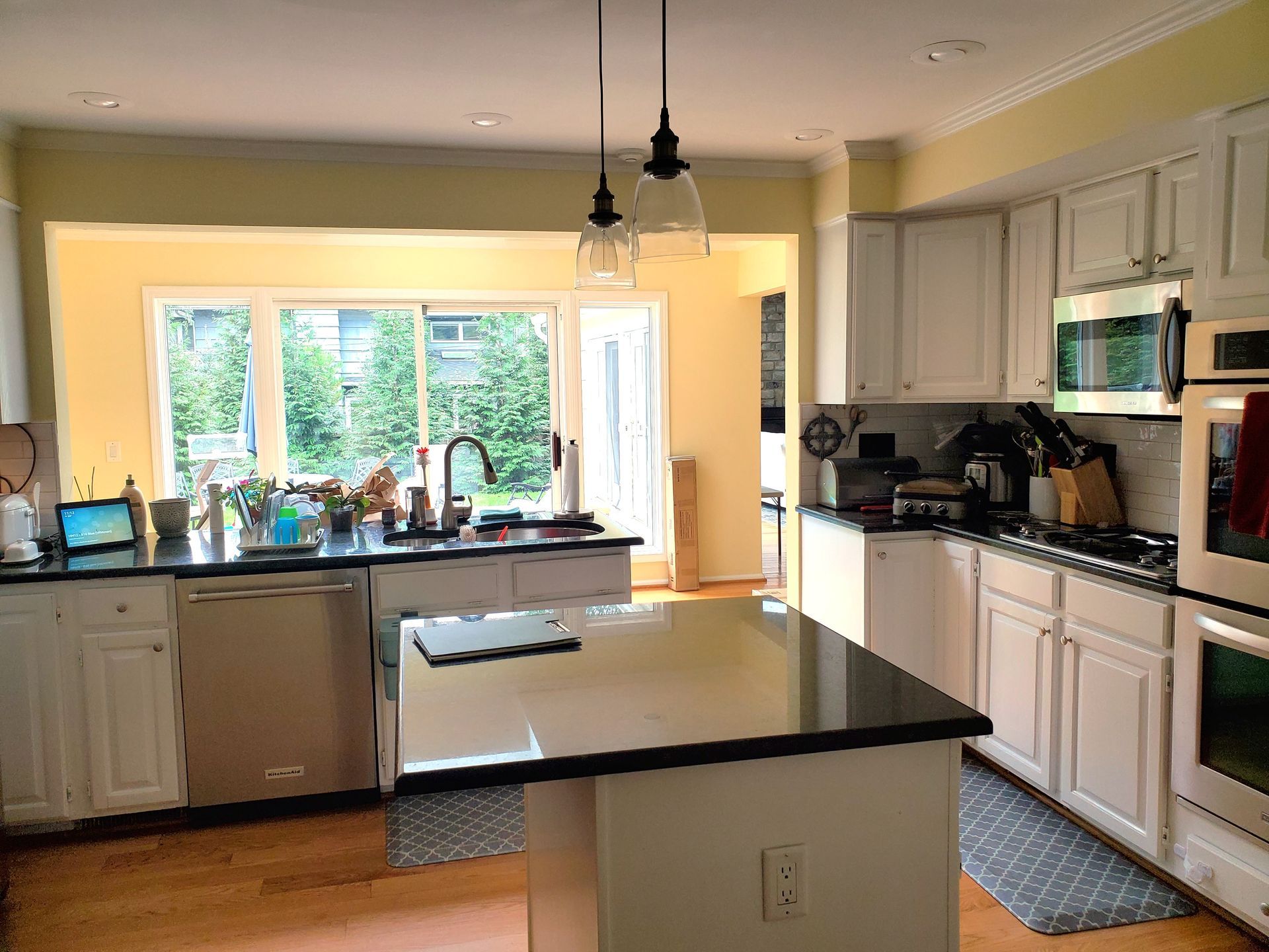Bright kitchen with white cabinets, black countertops, center island, and a large window over the sink.