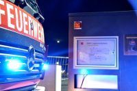 Ein Feuerwehrauto mit Blaulicht an der Vorderseite steht neben einem Gebäude.