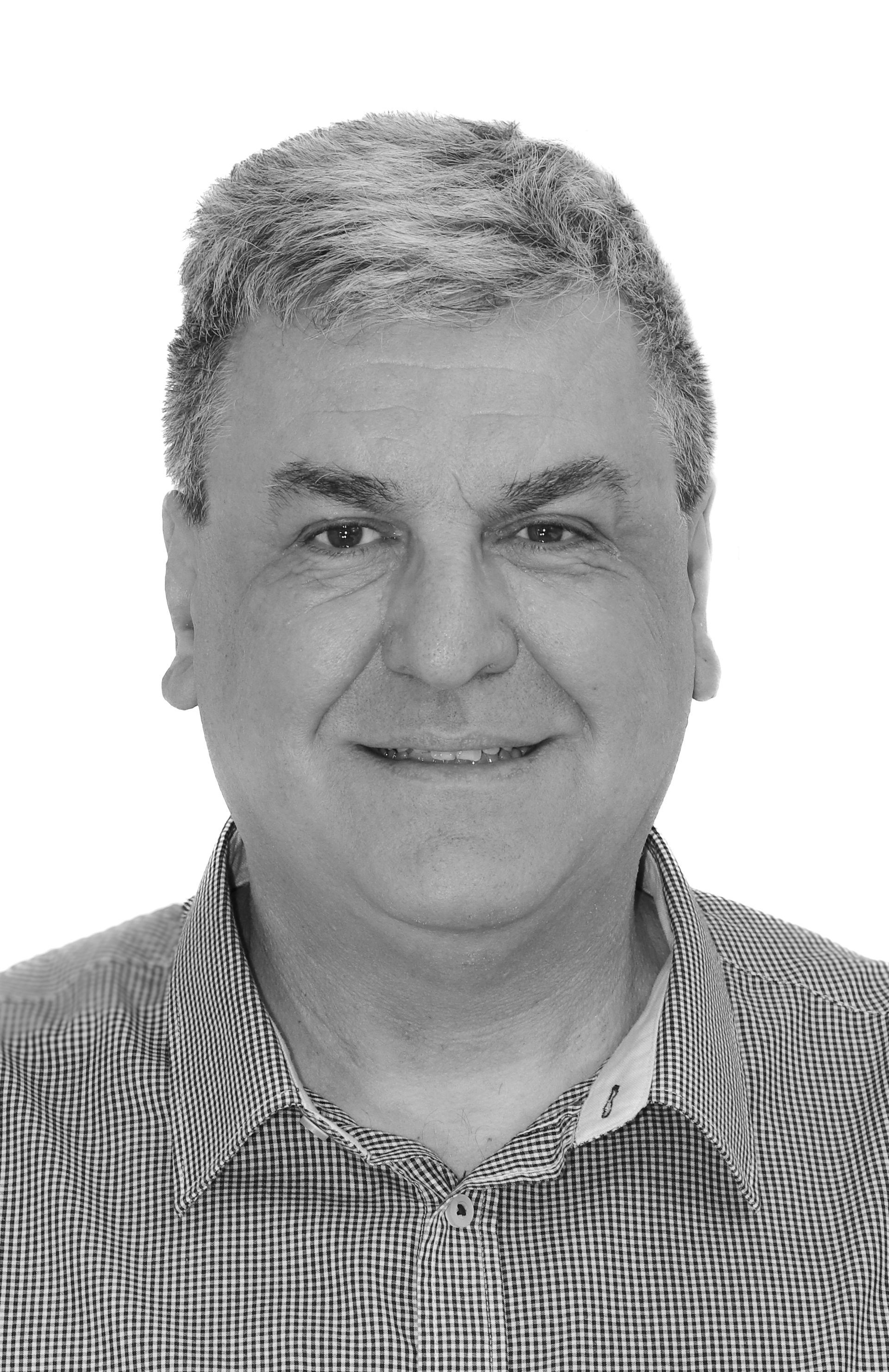 Auf einem Schwarzweißfoto lächelt ein Mann im karierten Hemd.