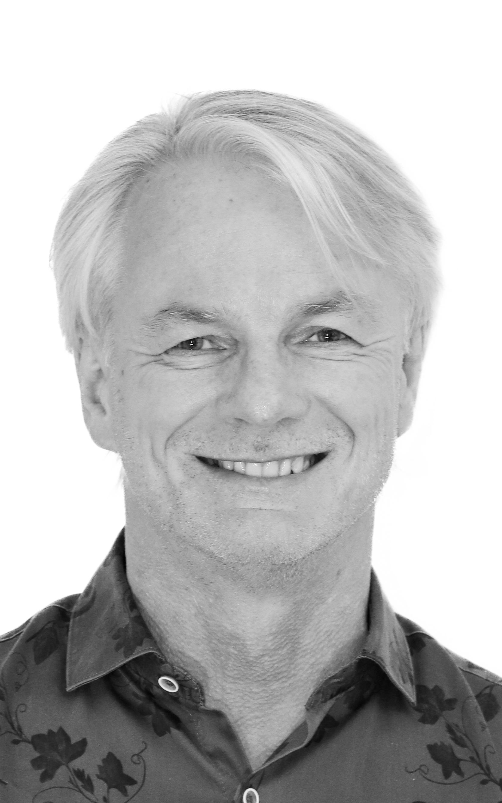 Ein Mann mit weißem Haar lächelt auf einem Schwarzweißfoto.