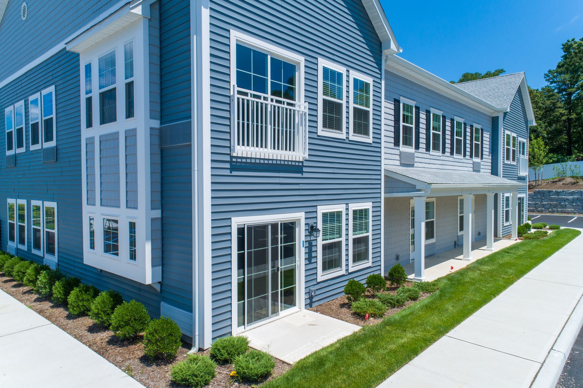 Blue and white multi-unit residential building with white windows, grass, and a sidewalk.