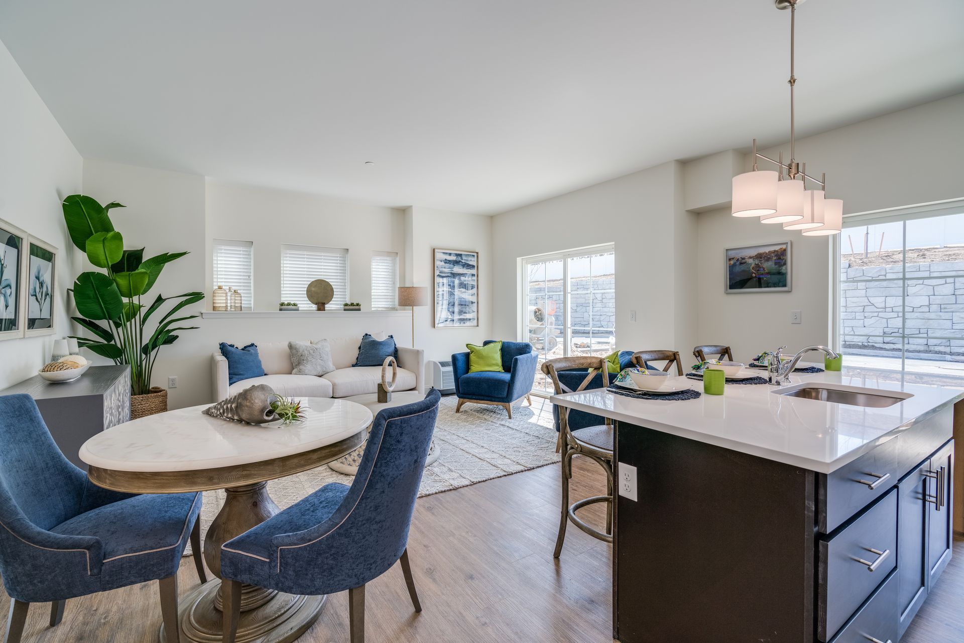 Open-concept living space with dining area, kitchen island, white walls, and blue accent furniture.