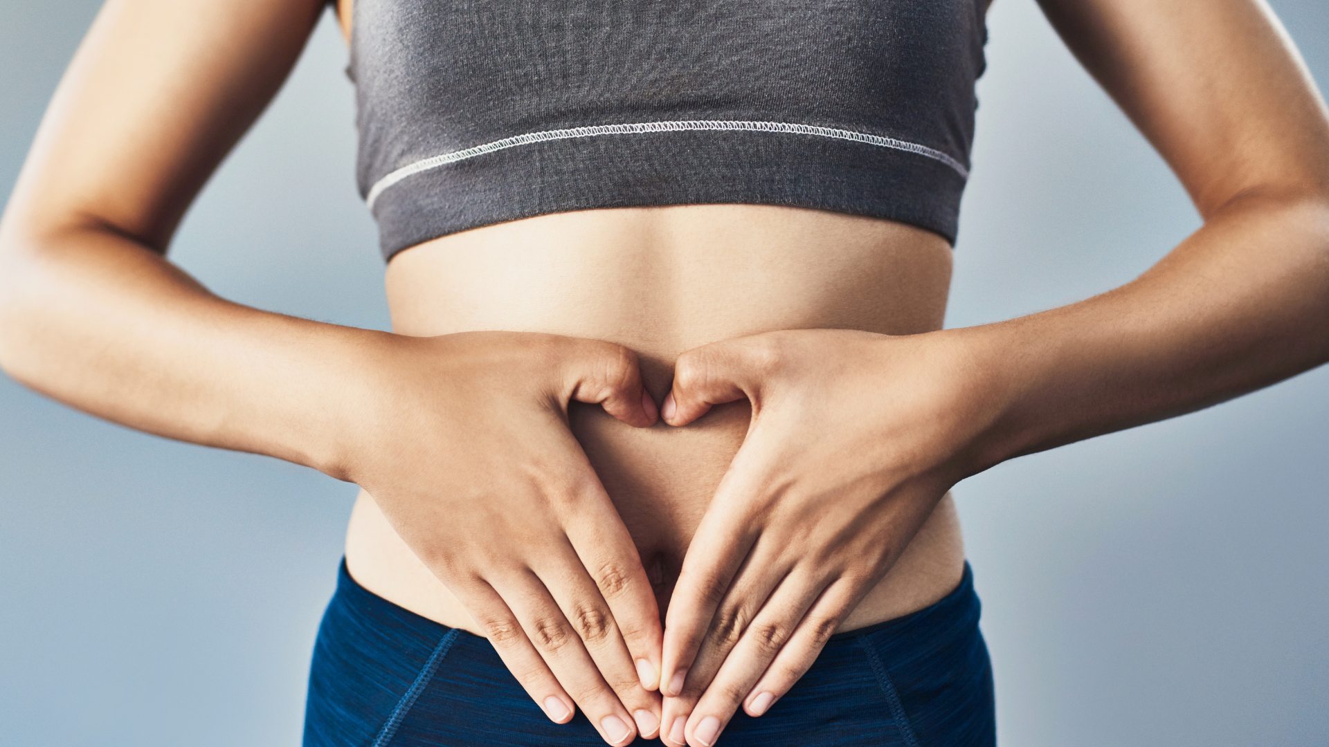 Woman in workout clothes with hands forming a heart over her abdomen.