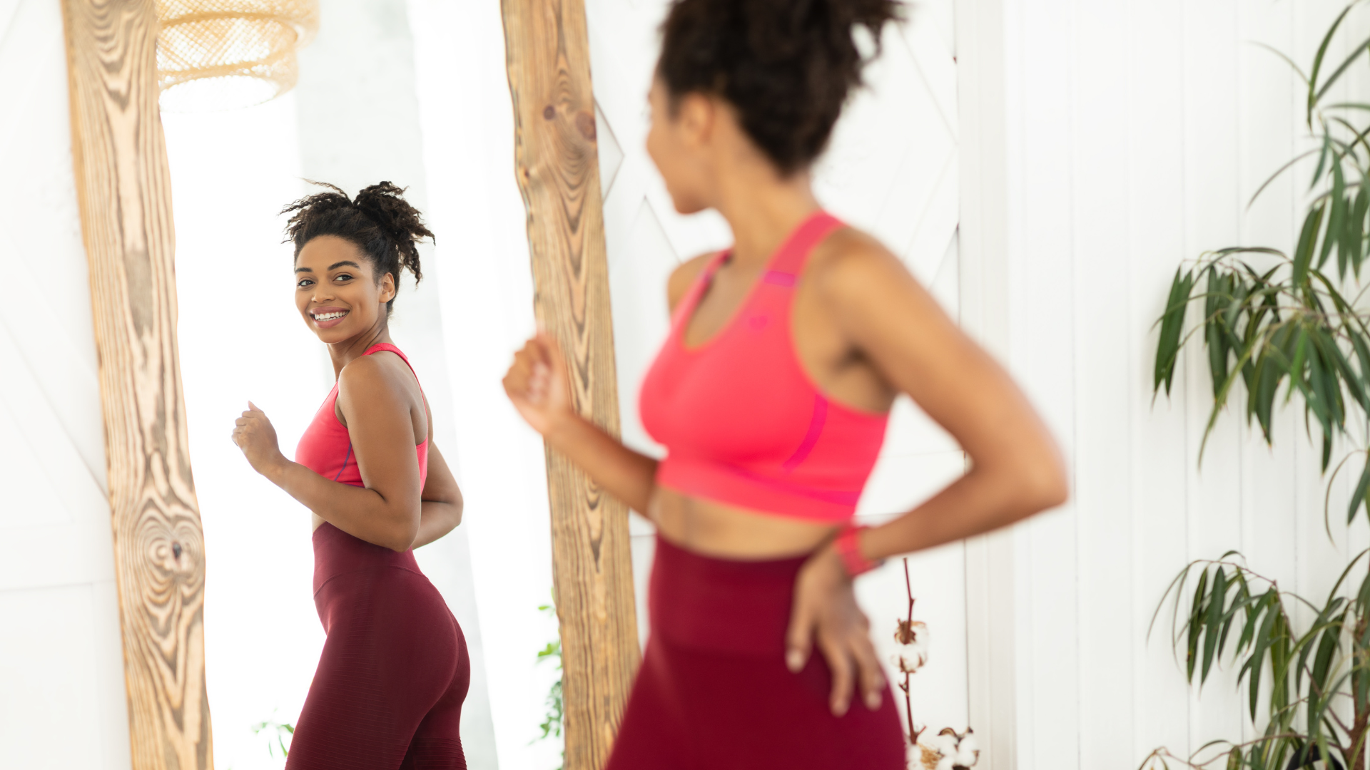 Woman in workout clothes smiles at herself in a mirror.