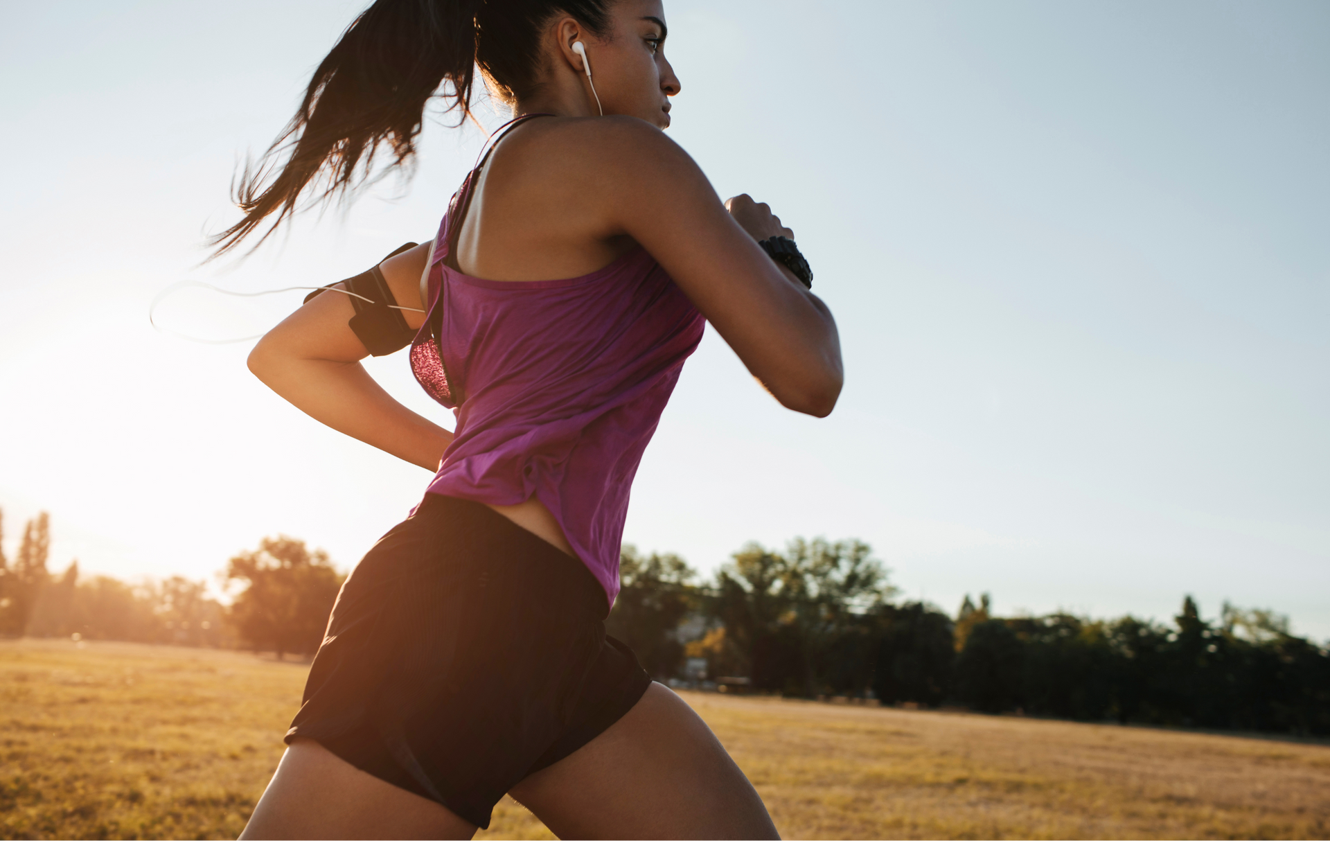 Woman running in a park, wearing athletic clothes, with the sun setting in the background.