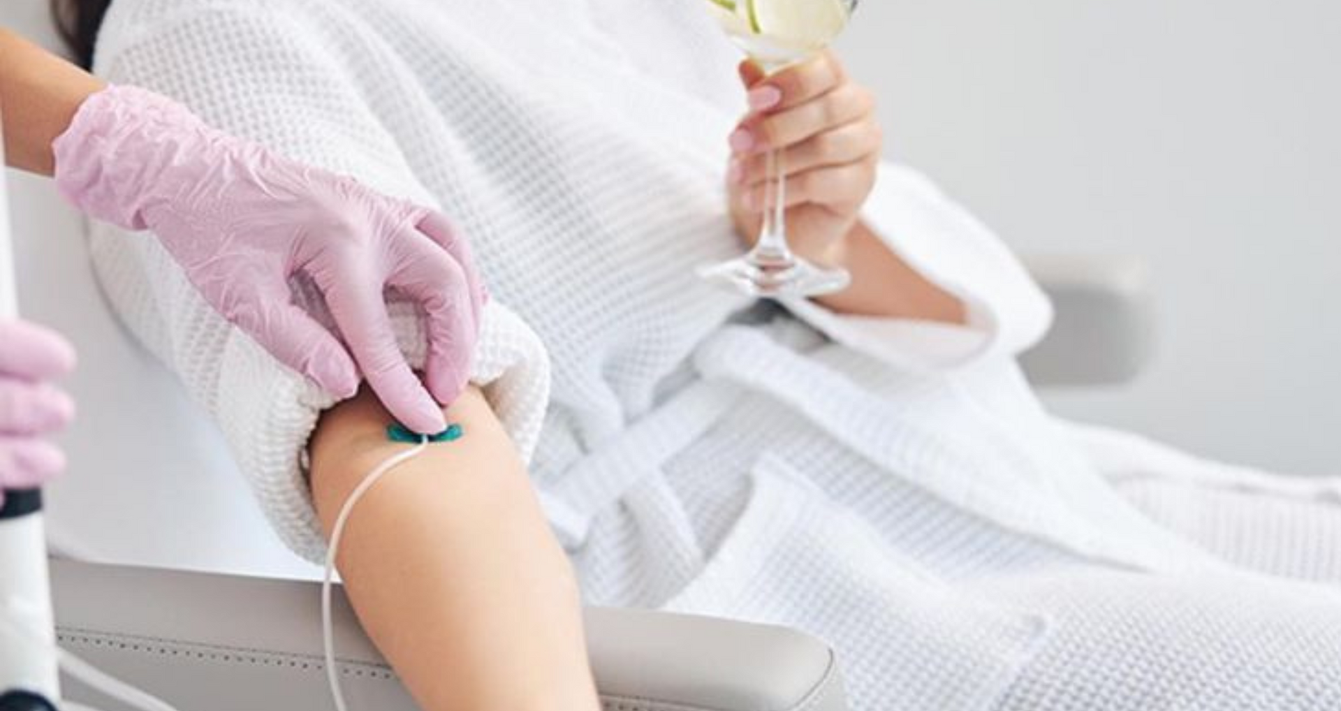 Person receiving an IV treatment while holding a drink, in a spa setting.