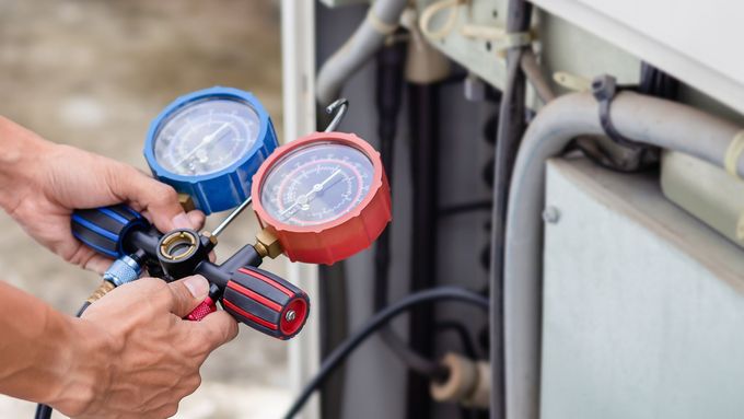 A technician holding a red and blue manifold gauge set while servicing an AC unit.