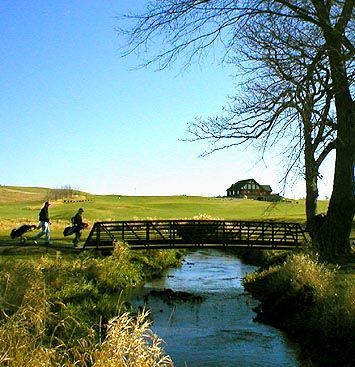 A bridge over a stream with a barn in the background