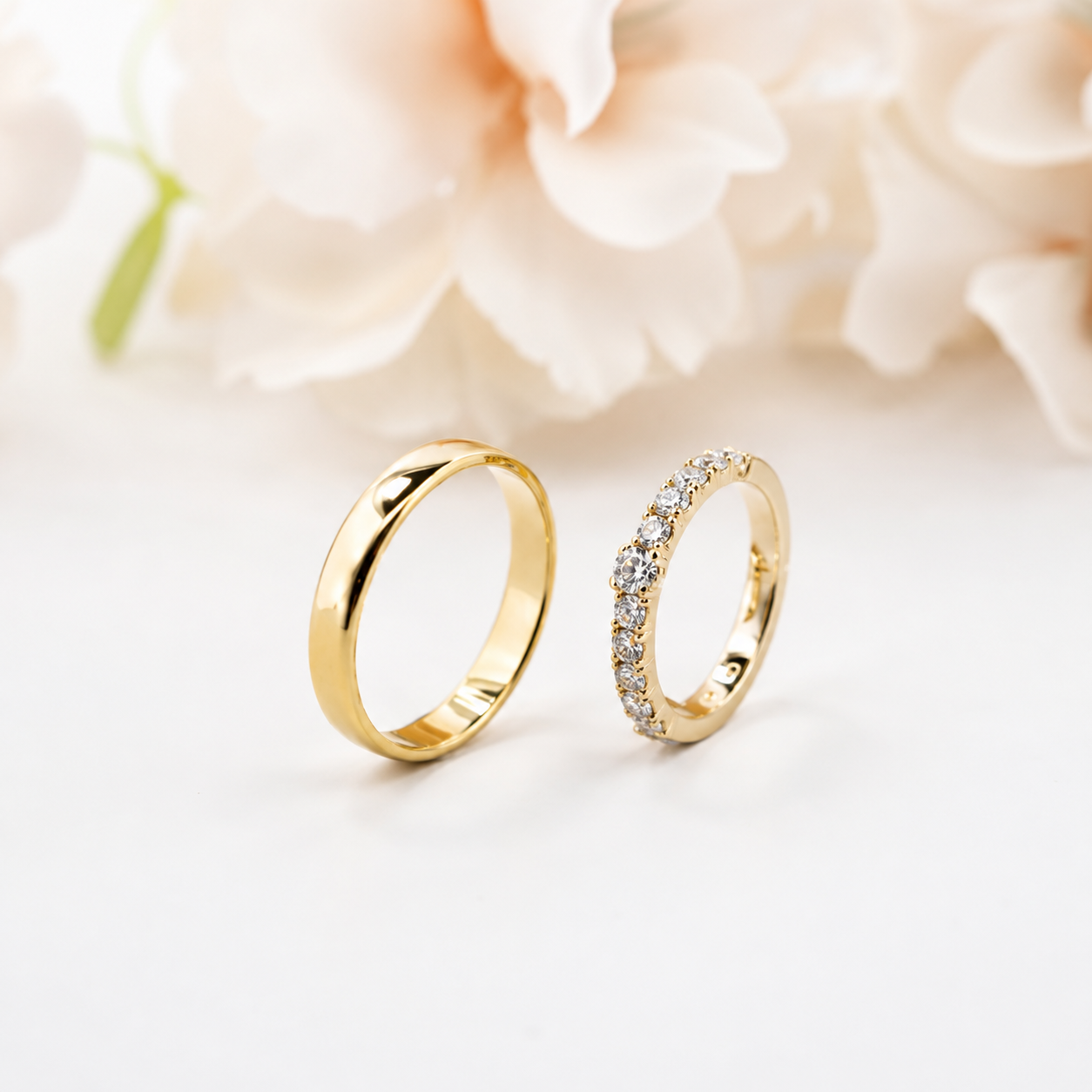 Twee gouden ringen op een zachtwitte ondergrond met wazige witte bloemen op de achtergrond.