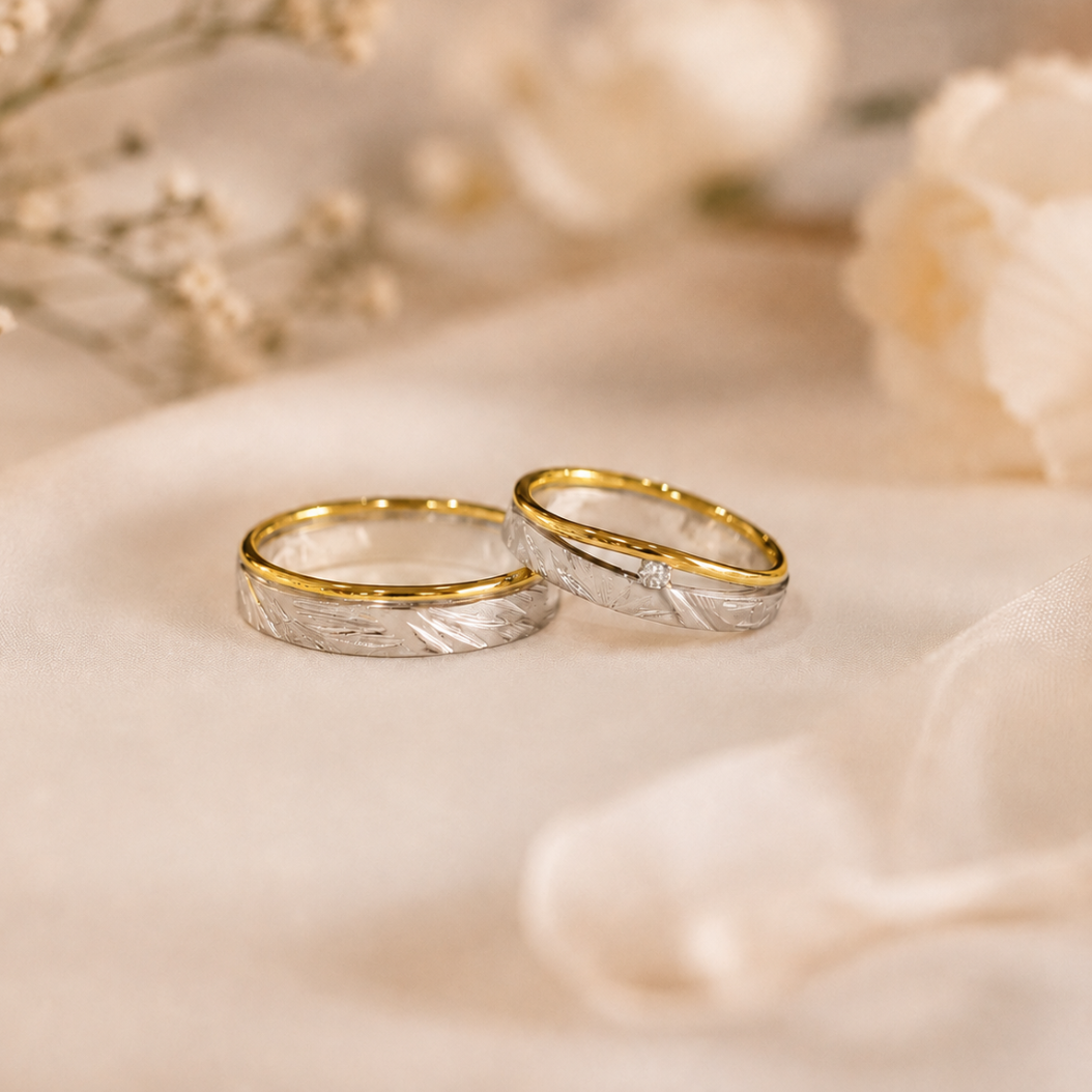 Twee bicolor gouden trouwringen met diamant op een zachtbeige stoffen achtergrond.