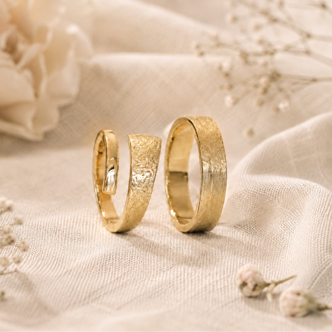Twee gouden ringen op een zachtbeige stof met delicate gedroogde bloemen eromheen.