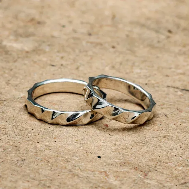 Twee witgouden ringen met golvende randen rusten op een lichtbruin, gestructureerd oppervlak.