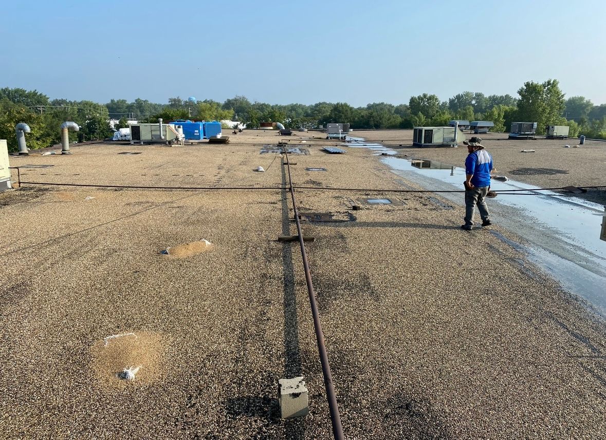 Person walking on a gravel rooftop near puddles and equipment under a clear sky