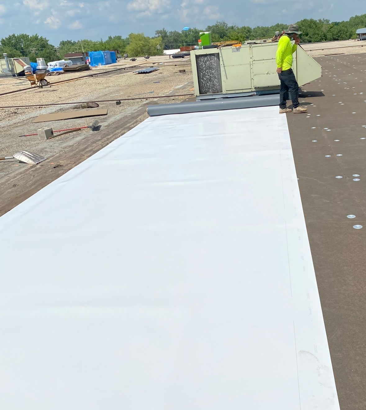 Worker installing a white rooftop membrane on a flat roof near HVAC units