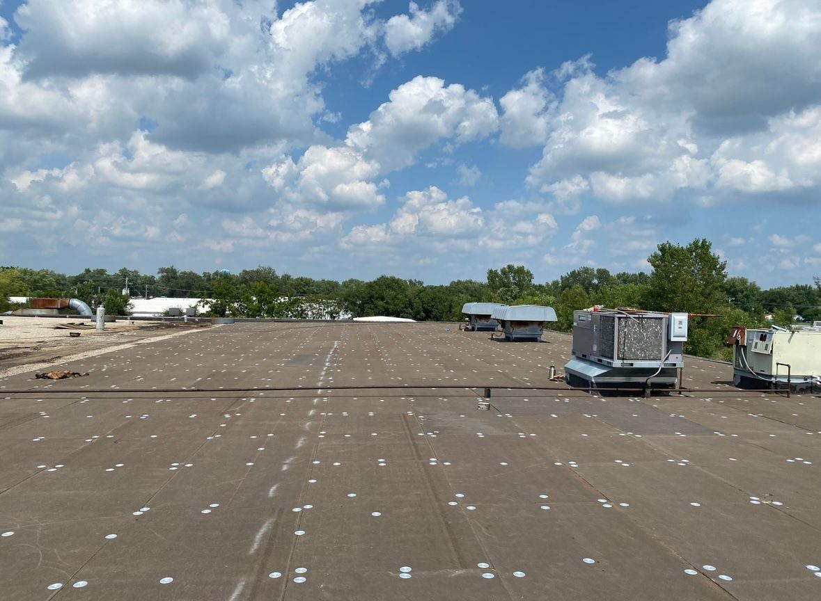 Flat rooftop with HVAC units under a partly cloudy blue sky.