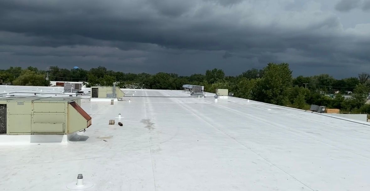 White flat rooftop under dark storm clouds with trees in the distance