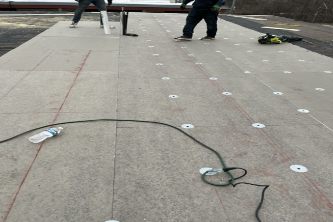 Rooftop work area with two workers, hoses, and tools on a flat surface with white marker spots.