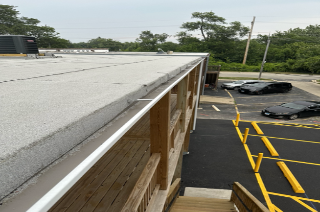 Rooftop edge with shingles beside a parking lot and wrapped equipment below