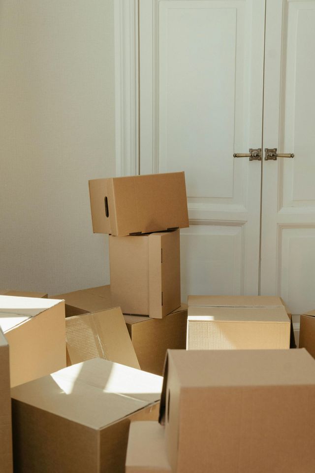Cardboard moving boxes stacked near a white door, suggesting relocation.