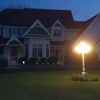 A house at night with a bright lamppost illuminating the lawn.