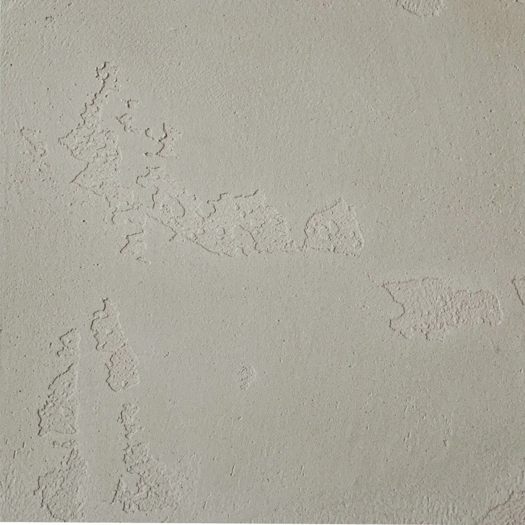 Close-up of a beige textured wall with peeling or chipped plaster patches