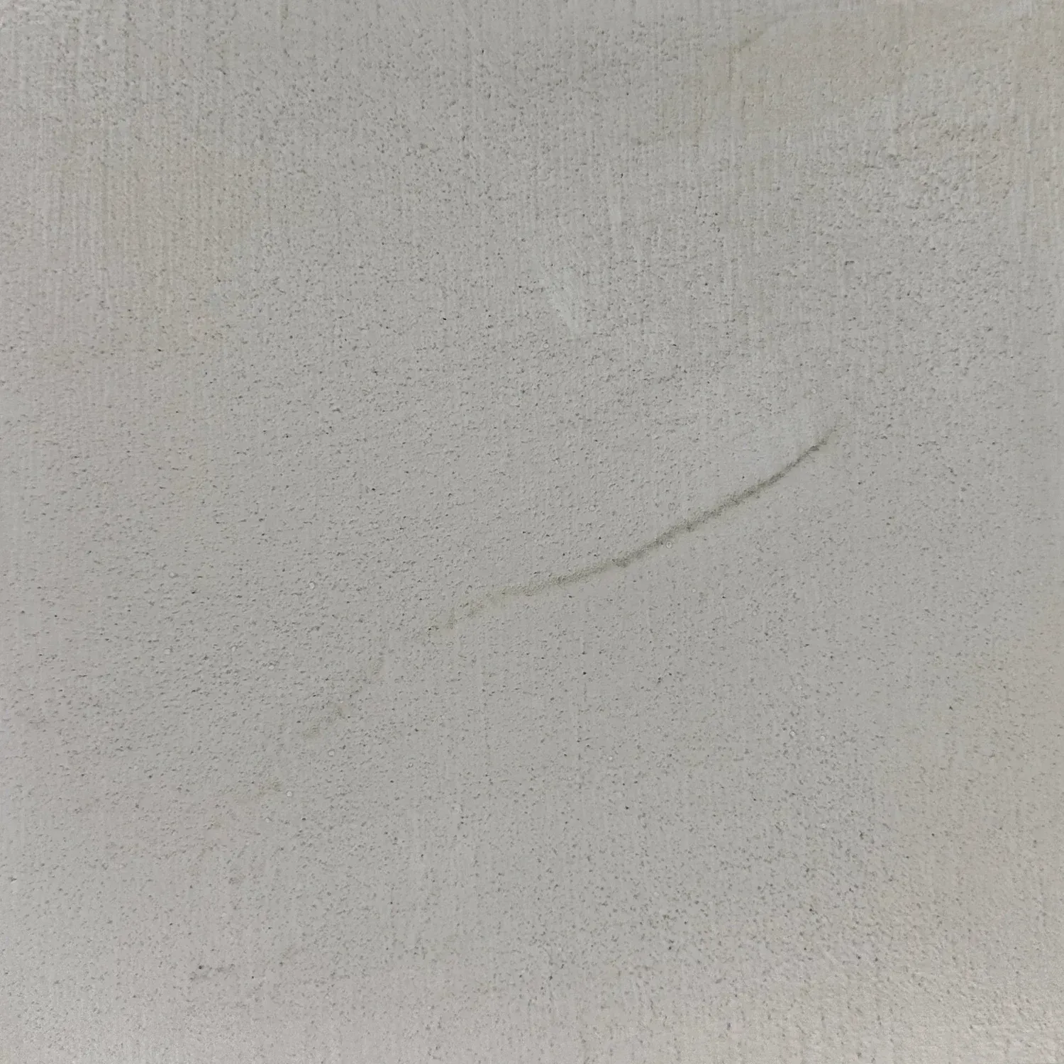 Close-up of a light gray textured surface with a faint curved scratch or stain.