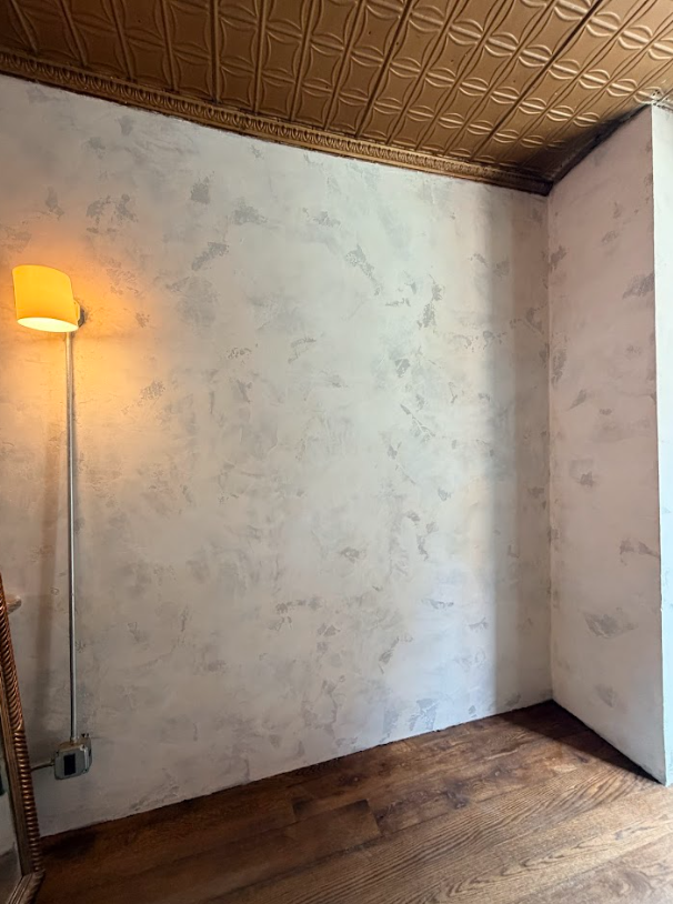 Empty room with white walls, wood floor, woven ceiling, and a lit floor lamp in the corner.