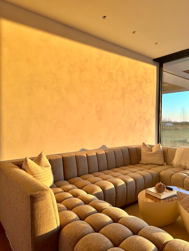 Sunlit beige tufted sectional by a large window in a modern living room