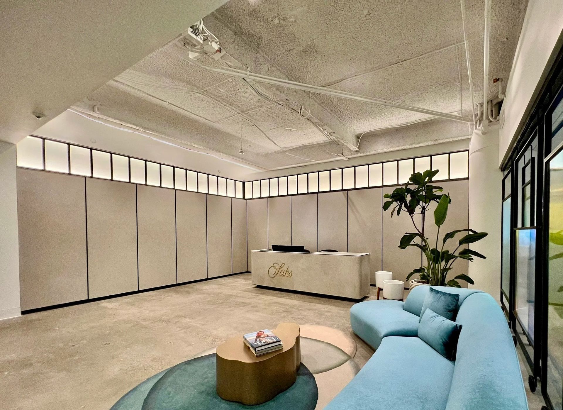 Modern office reception area with light blue sofa, reception desk, and large windows.