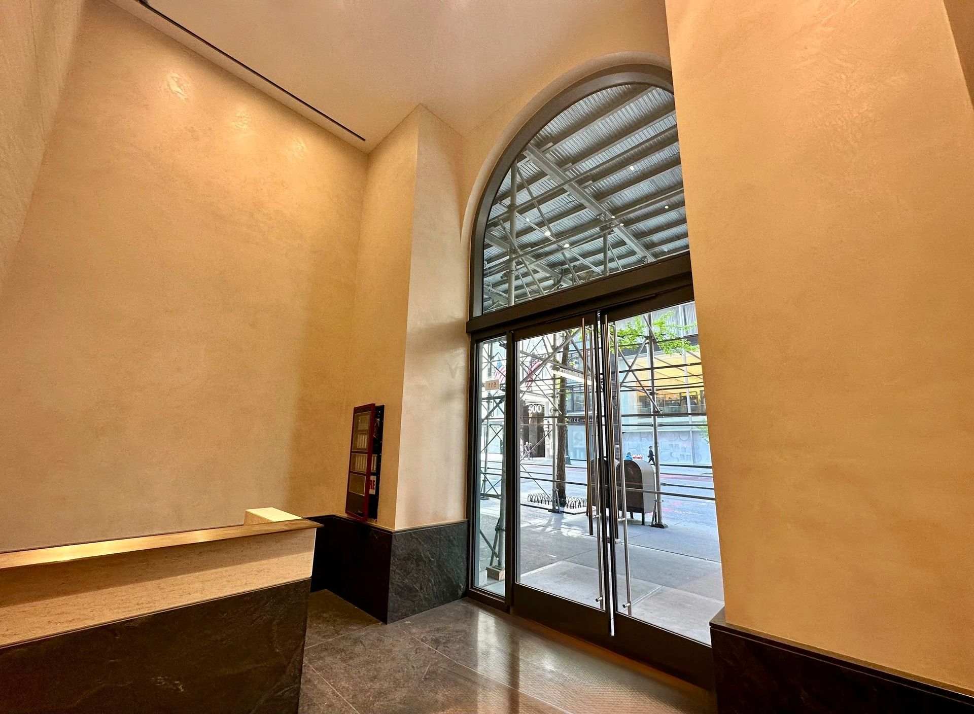 Entrance to a building with glass doors, arched window, and beige walls.
