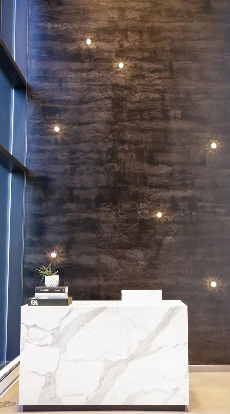 Marble reception desk against a textured dark wall with small lights. A plant and books sit on the desk.