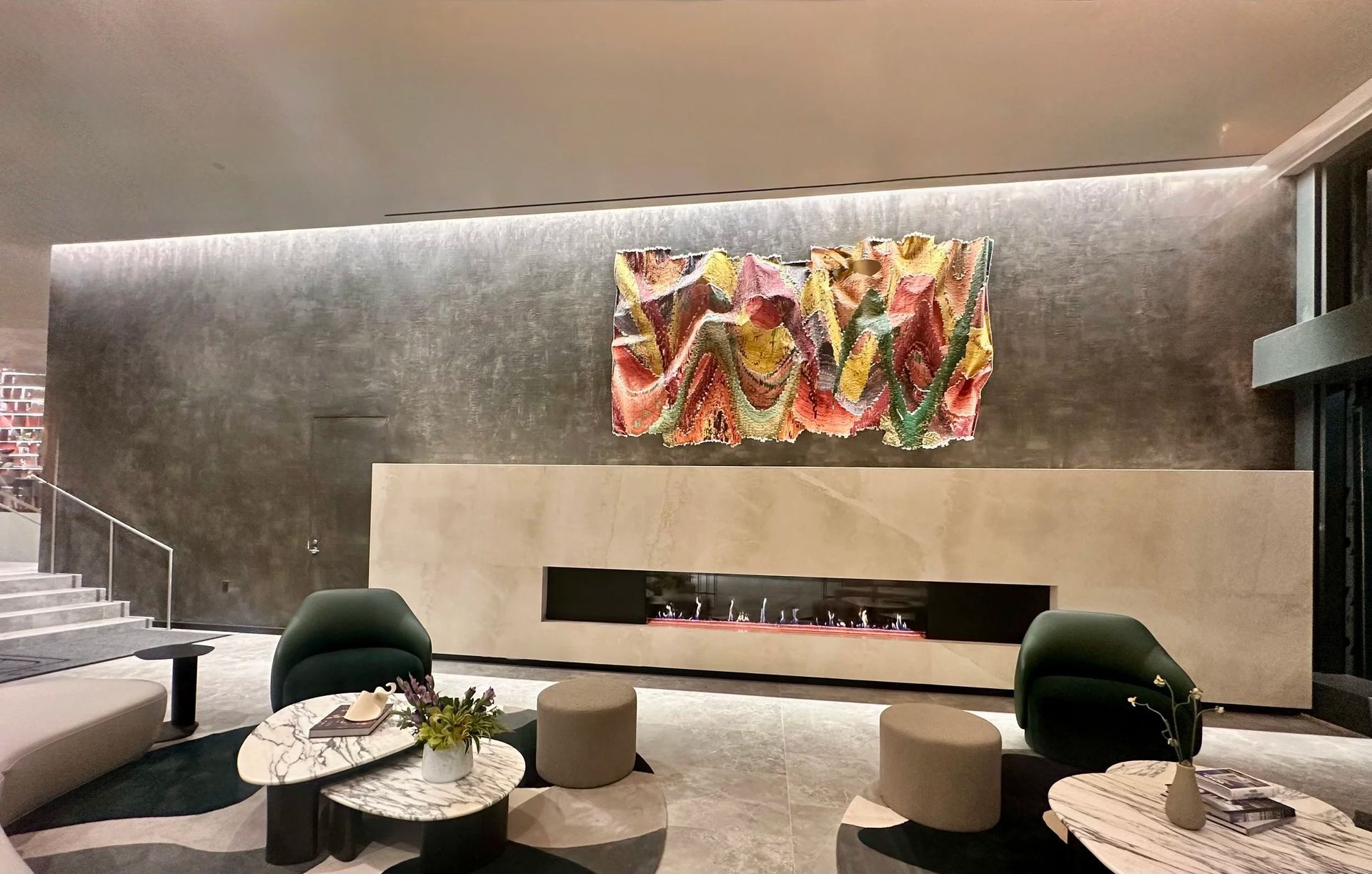 Modern lounge with fireplace, abstract art, green chairs, and marble coffee tables.