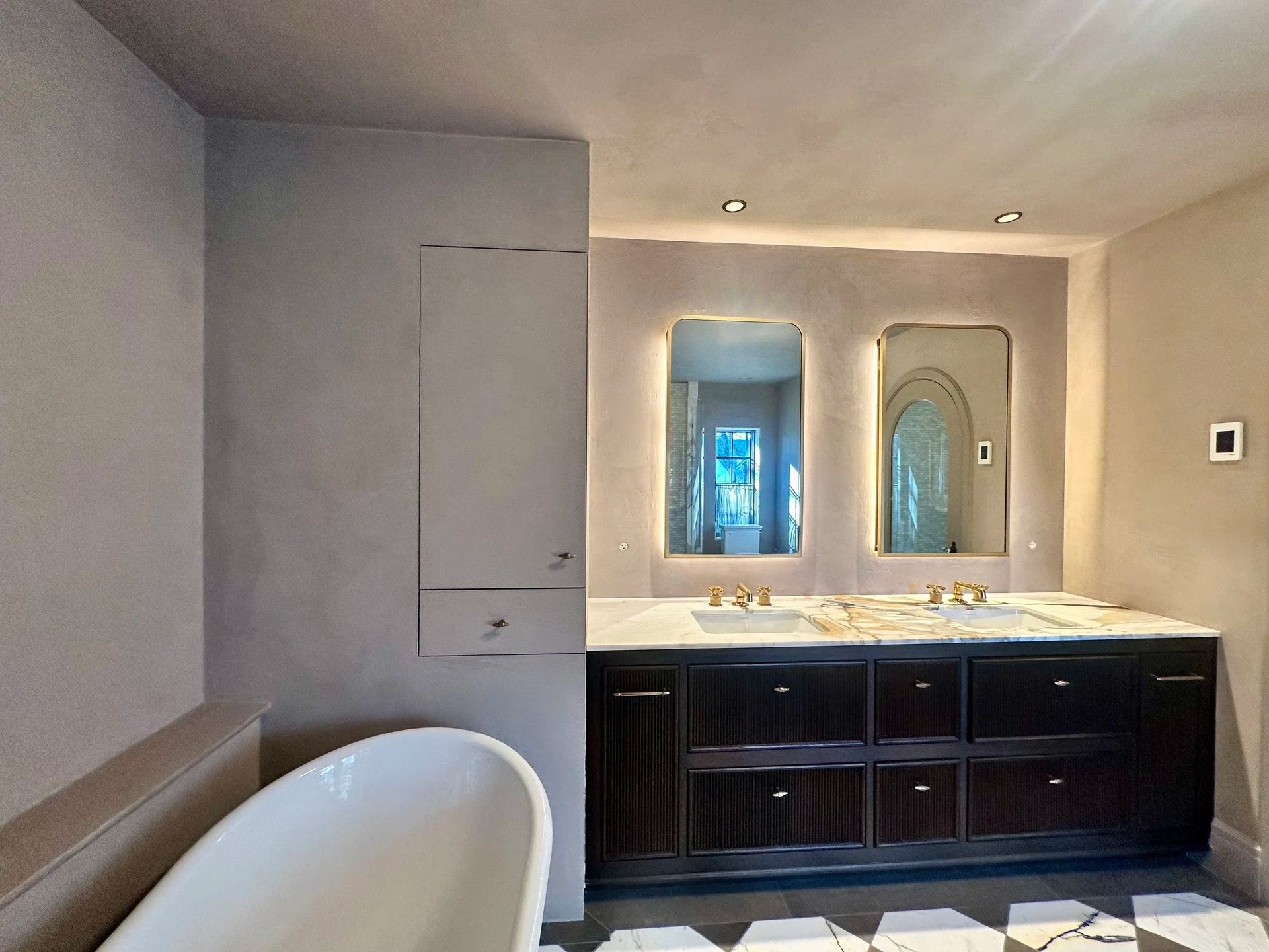 Modern bathroom with a dark wood vanity, illuminated mirrors, and a freestanding tub.
