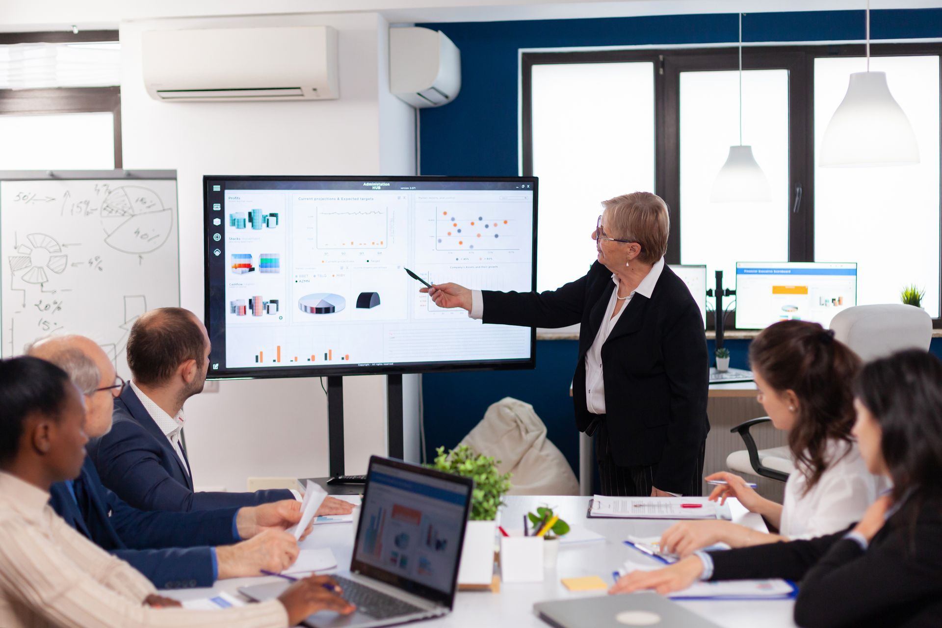Office meeting with three people, colorful sticky notes on a board, rising chart, and stacked folders in the foreground